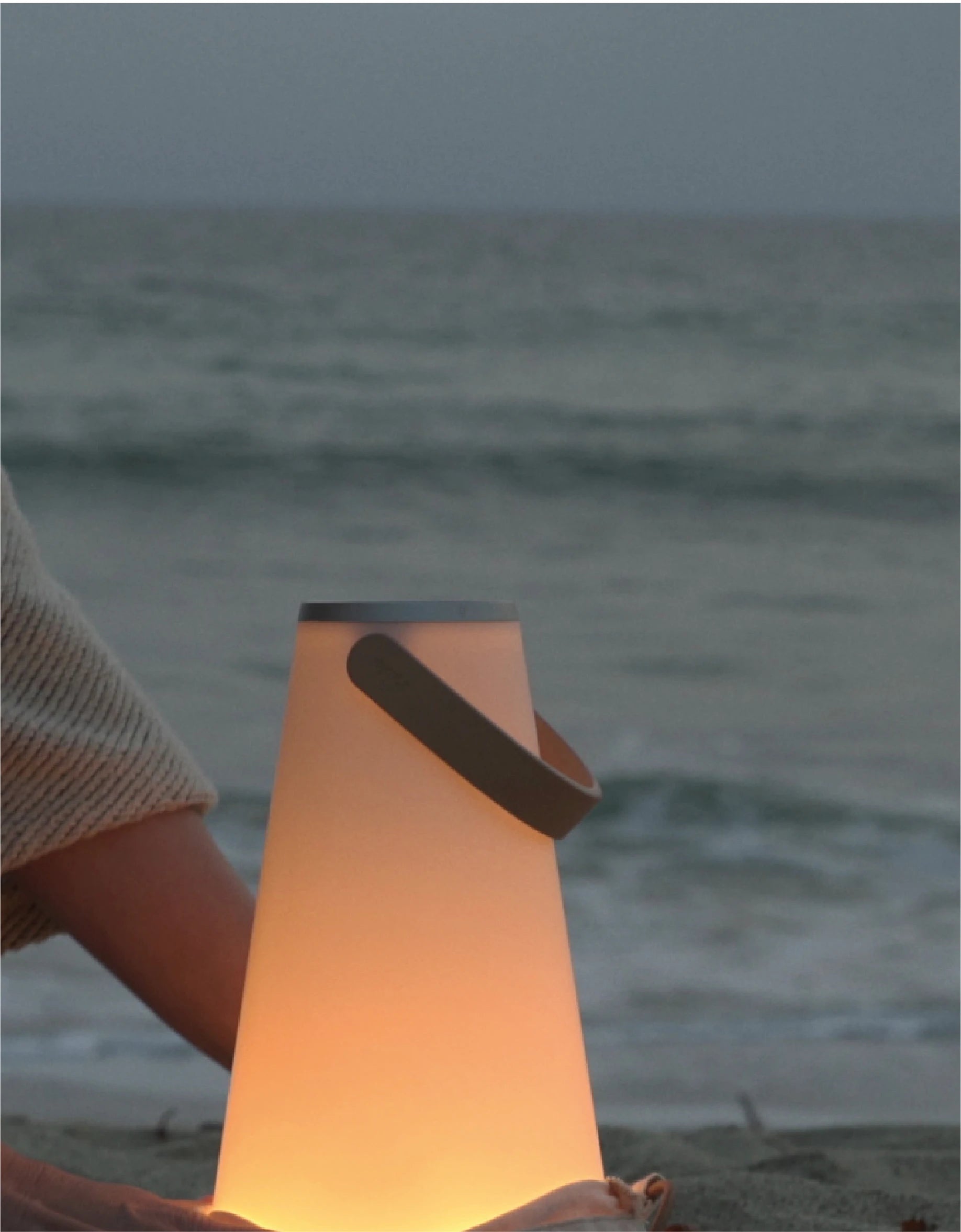 Luminous lantern held by a person on a beach with ocean in the background
