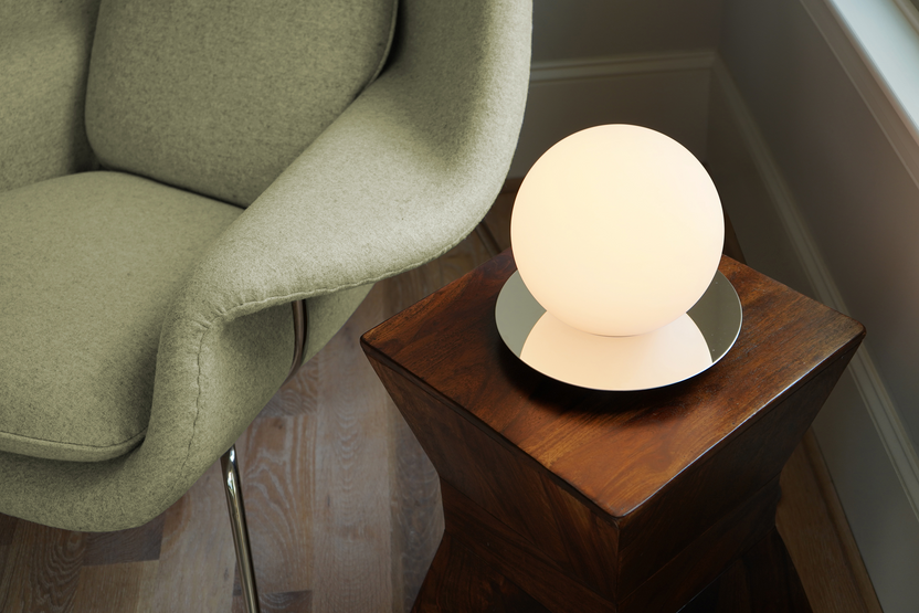 Round table lamp on a wooden side table next to a green armchair