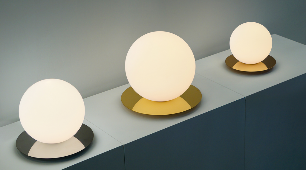 Three spherical table lamps with different base colors on a gray surface.