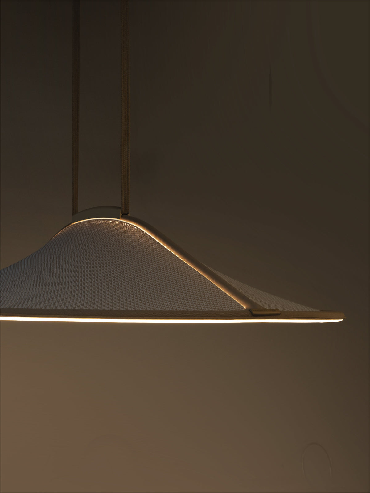 A modern pendant light with a wide, shallow conical shade made of textured white fabric, suspended by thin dark rods. The light is turned on, casting a warm glow along the bottom edge against a dark, minimalist background.